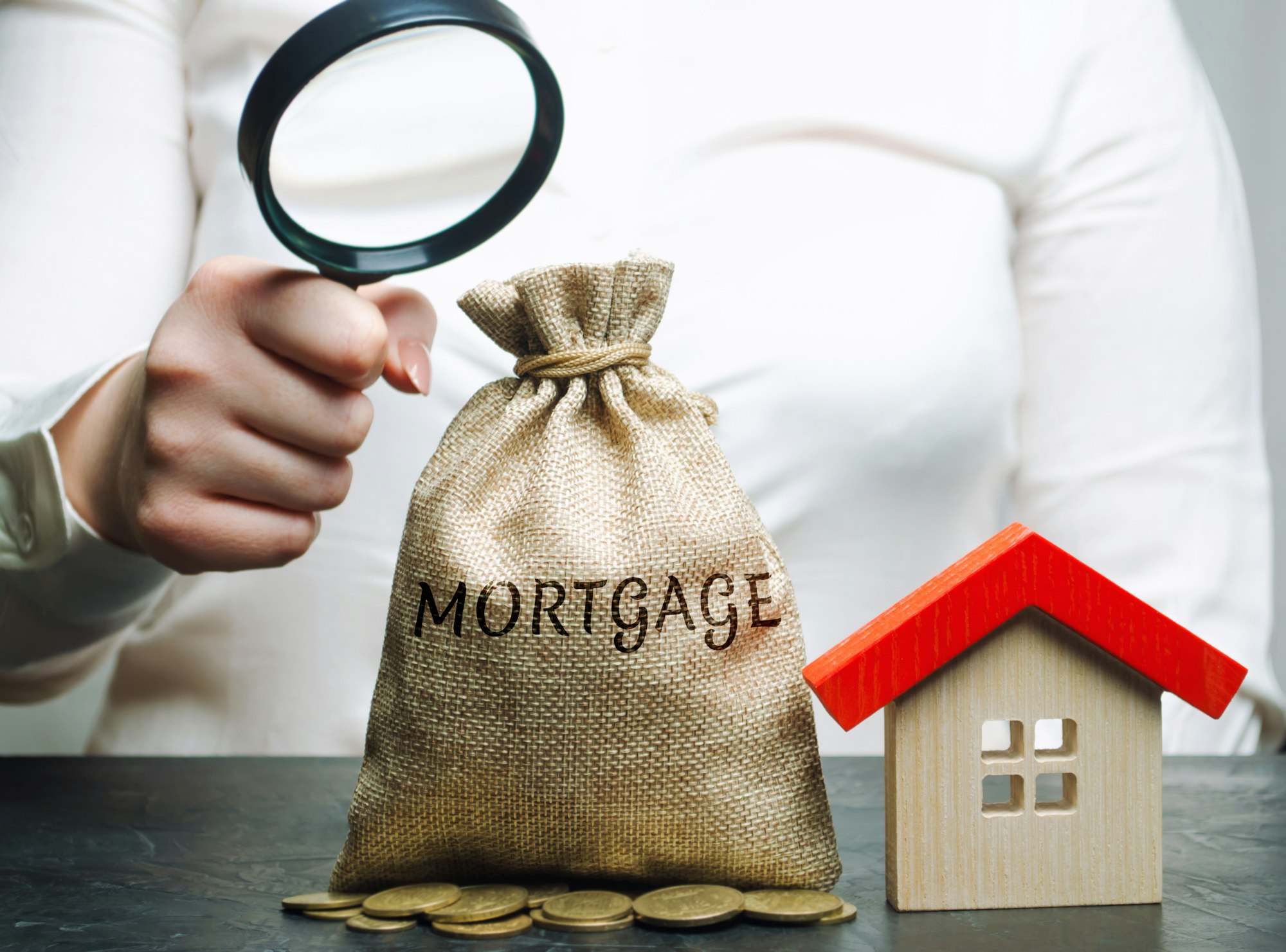 A female hand is holding a magnifying glass over a money bag with the word Mortgage and a wooden